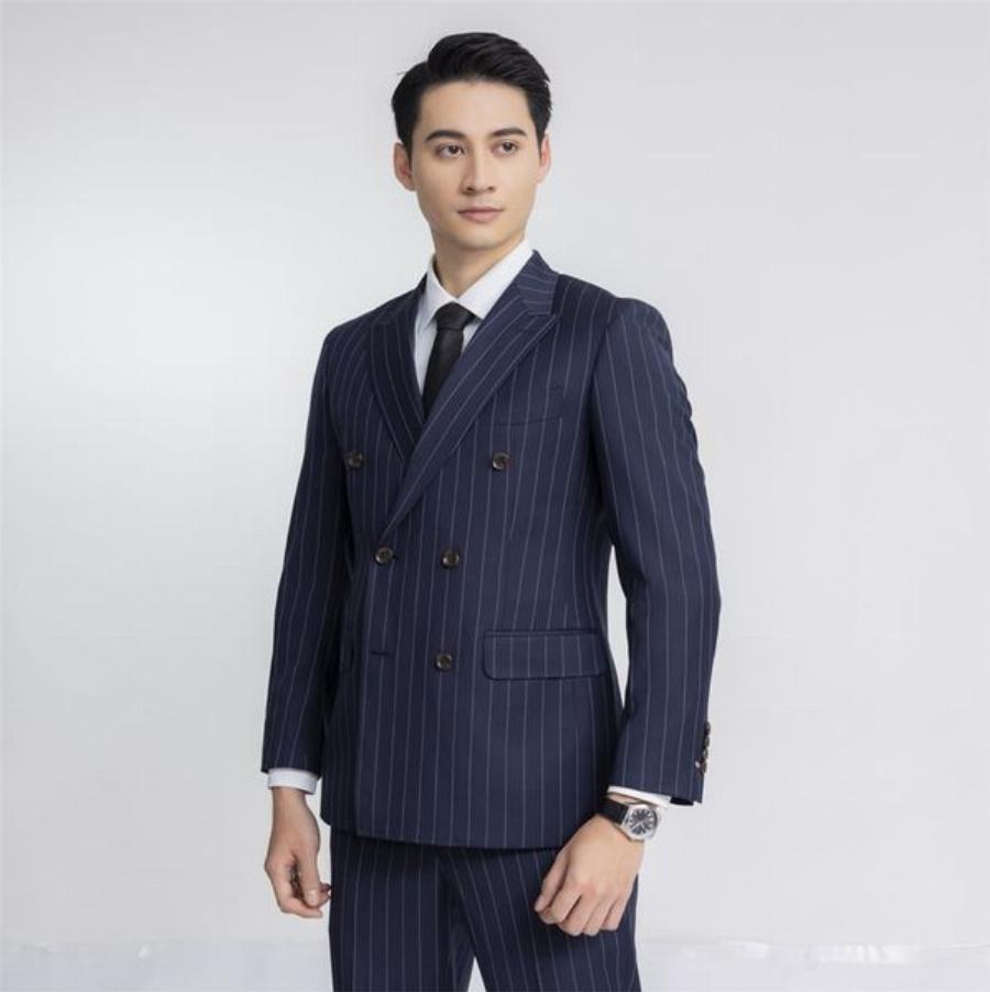 Người đàn ông Việt Nam mặc bộ đồ công sở Aristino gồm áo sơ mi trắng, quần tây xanh navy và thắt lưng da, đứng trong không gian cửa hàng Aristino Vincom Quảng Ngãi